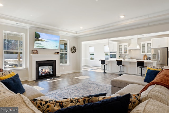 living room featuring baseboards, a multi sided fireplace, light wood-style flooring, and crown molding