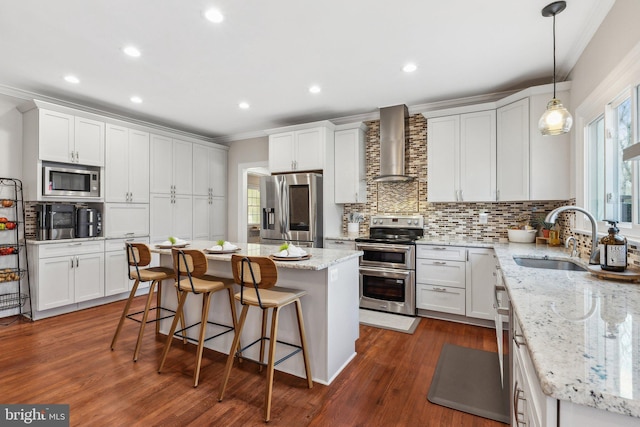 kitchen featuring a kitchen island, wall chimney range hood, ornamental molding, appliances with stainless steel finishes, and a sink