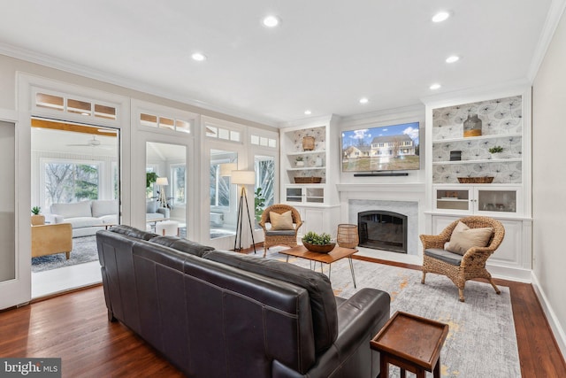 living room with built in features, recessed lighting, a fireplace, dark wood-style flooring, and crown molding