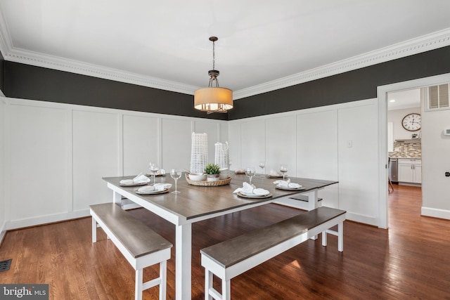 dining space with wood finished floors, ornamental molding, and a decorative wall