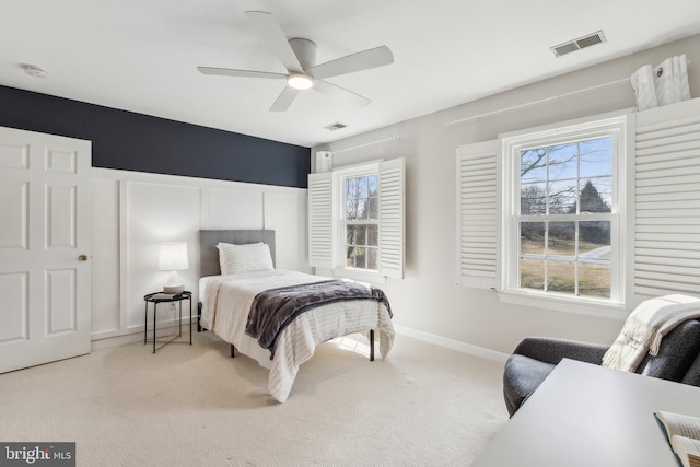 bedroom featuring a decorative wall, carpet flooring, a ceiling fan, and visible vents