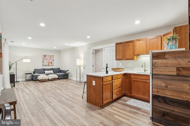 kitchen with light wood finished floors, open floor plan, a kitchen bar, a peninsula, and a sink