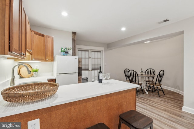 kitchen featuring a sink, freestanding refrigerator, brown cabinetry, light wood finished floors, and light countertops