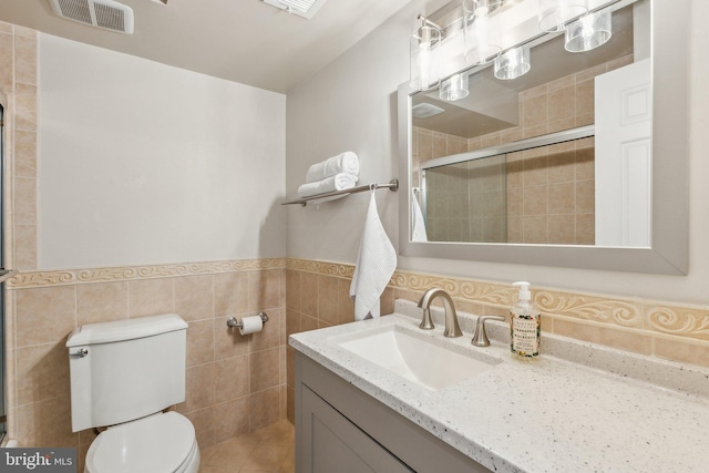 full bathroom featuring visible vents, a wainscoted wall, toilet, a tile shower, and tile walls