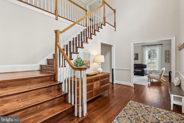 staircase featuring baseboards, a high ceiling, and wood finished floors