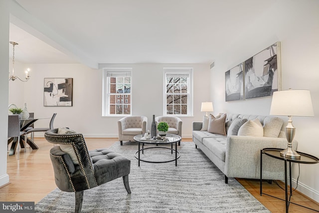 living room with visible vents, an inviting chandelier, baseboards, and wood finished floors