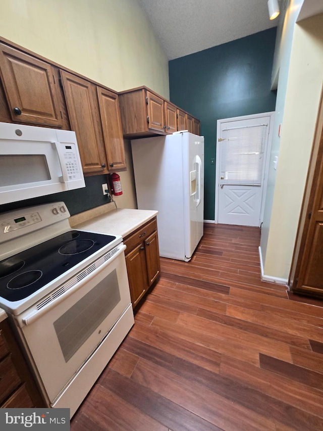 kitchen with white appliances, dark wood-style floors, light countertops, vaulted ceiling, and a textured ceiling