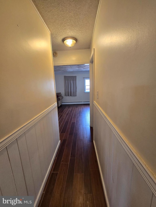 hallway featuring dark wood finished floors, a wainscoted wall, a textured ceiling, and a baseboard radiator