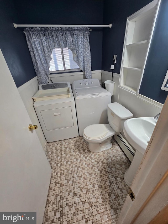 bathroom with washing machine and clothes dryer, a baseboard heating unit, a wainscoted wall, toilet, and a sink