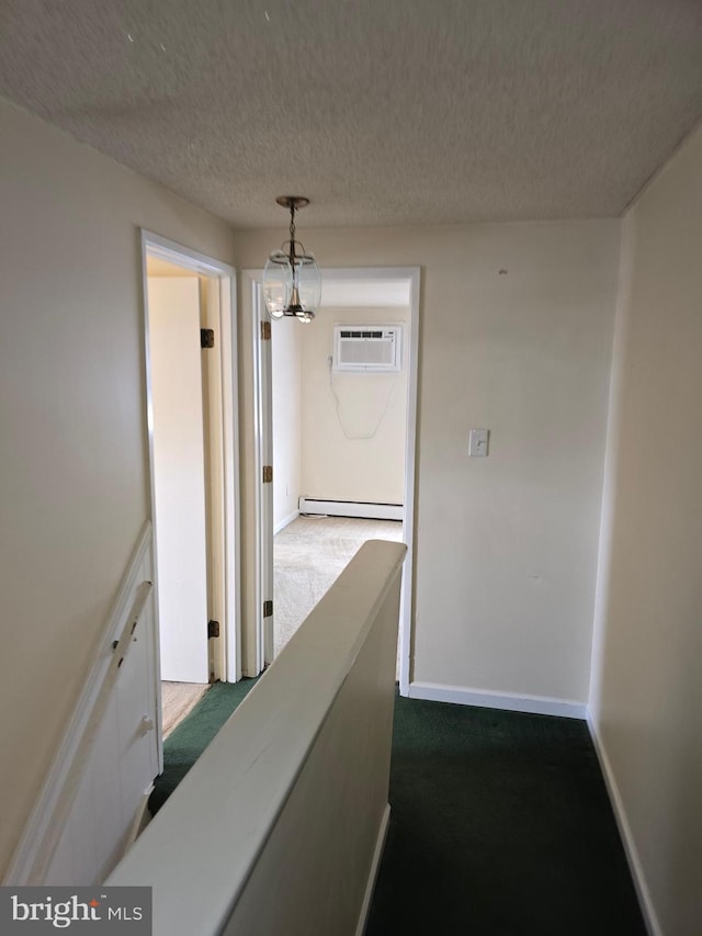 hallway featuring baseboards, a baseboard radiator, an AC wall unit, a textured ceiling, and dark colored carpet