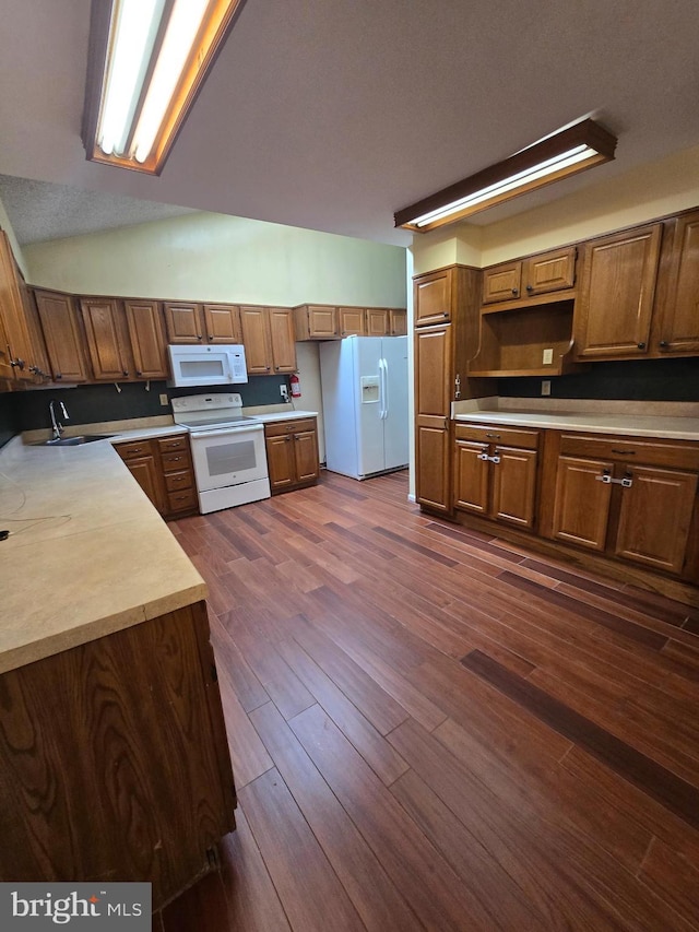 kitchen with brown cabinets, dark wood-type flooring, a sink, white appliances, and light countertops