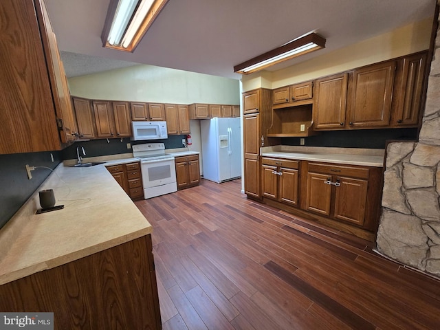 kitchen with light countertops, lofted ceiling, dark wood-style floors, white appliances, and a sink