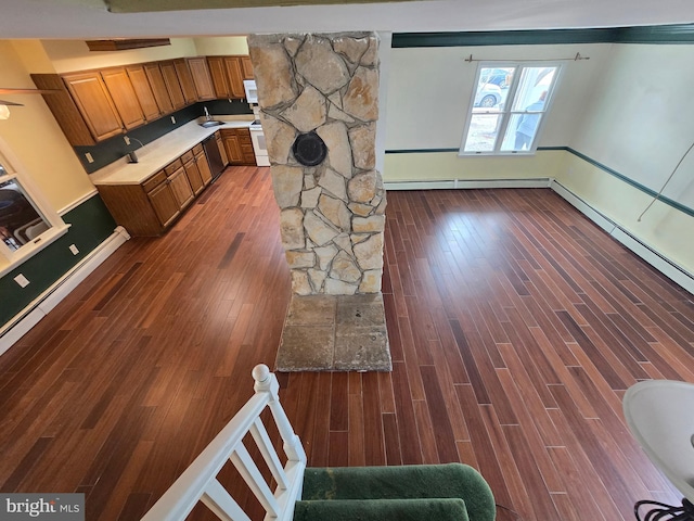 kitchen featuring light countertops, baseboard heating, wood finished floors, brown cabinetry, and a sink