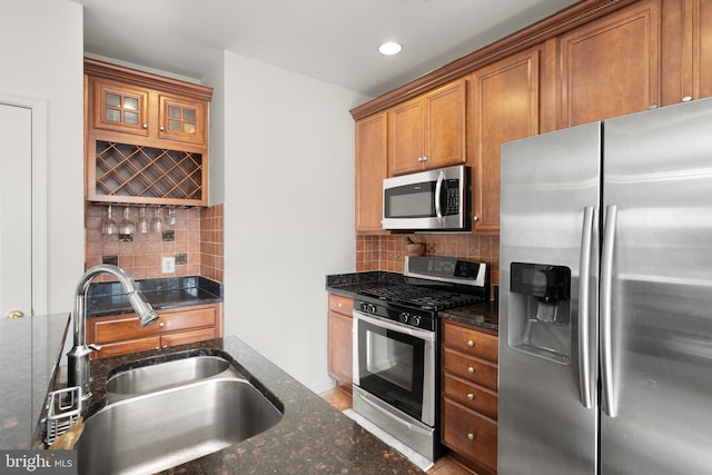 kitchen with a sink, dark stone countertops, stainless steel appliances, brown cabinetry, and decorative backsplash