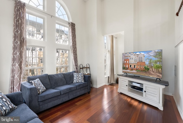 living area with dark wood-type flooring, baseboards, and a towering ceiling