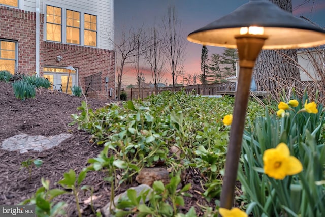 yard at dusk featuring a garden and fence