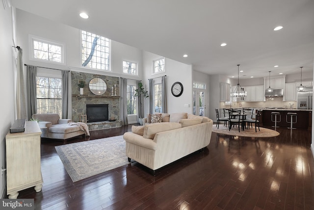 living area featuring a stone fireplace, plenty of natural light, dark wood-style floors, and recessed lighting