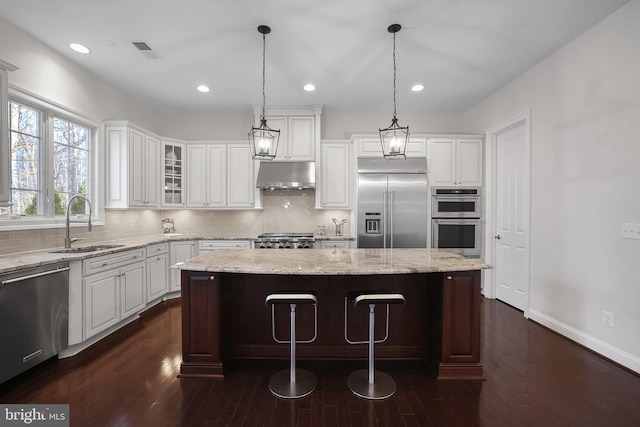 kitchen with visible vents, a sink, under cabinet range hood, appliances with stainless steel finishes, and a center island