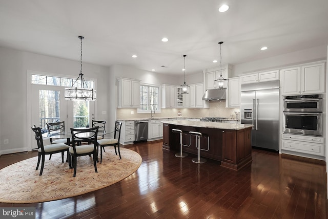 kitchen featuring a kitchen island, under cabinet range hood, decorative backsplash, appliances with stainless steel finishes, and dark wood-style floors