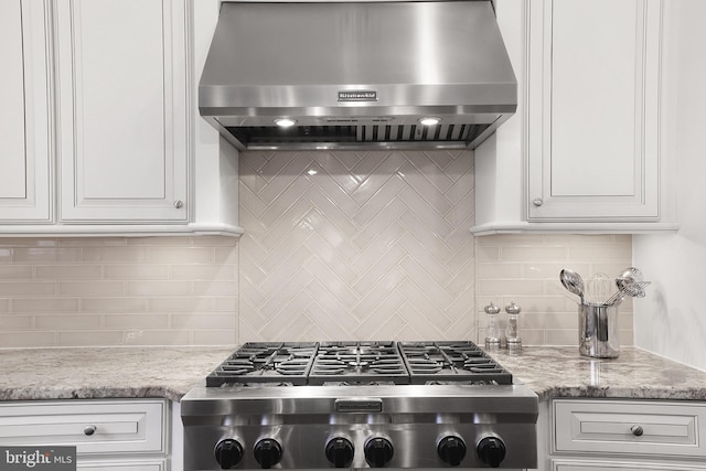 kitchen with light stone countertops, stainless steel gas cooktop, white cabinetry, exhaust hood, and backsplash