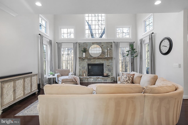 living area with dark wood finished floors, a stone fireplace, recessed lighting, and a high ceiling