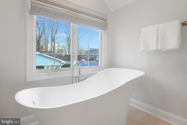 full bath with baseboards, a soaking tub, and lofted ceiling