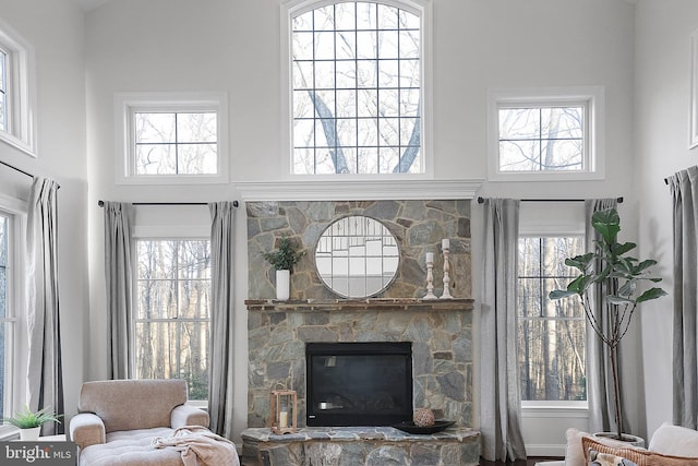 living room featuring a wealth of natural light, a stone fireplace, and a high ceiling