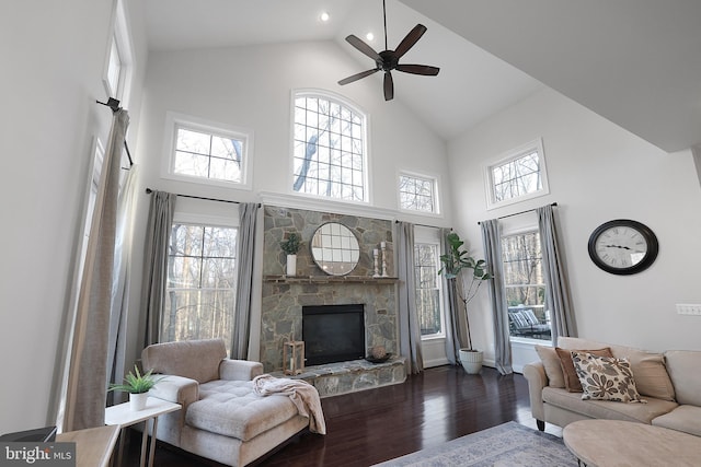 living room with ceiling fan, a stone fireplace, wood finished floors, and a healthy amount of sunlight