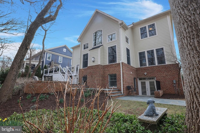 back of house with brick siding, a patio area, french doors, and stairs