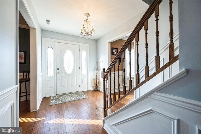 entryway with a wainscoted wall, hardwood / wood-style floors, stairway, a decorative wall, and a chandelier