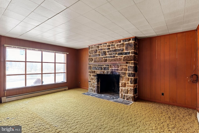 unfurnished living room with baseboard heating, wood walls, a stone fireplace, and carpet floors