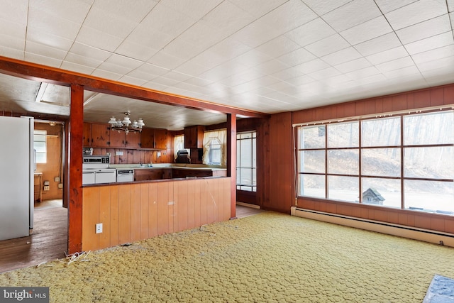 kitchen featuring a baseboard heating unit, freestanding refrigerator, wood walls, carpet flooring, and a chandelier