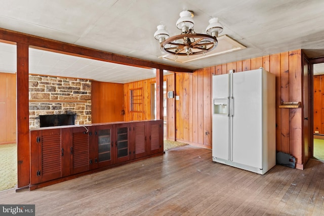 kitchen with a notable chandelier, wood walls, hardwood / wood-style floors, and white fridge with ice dispenser