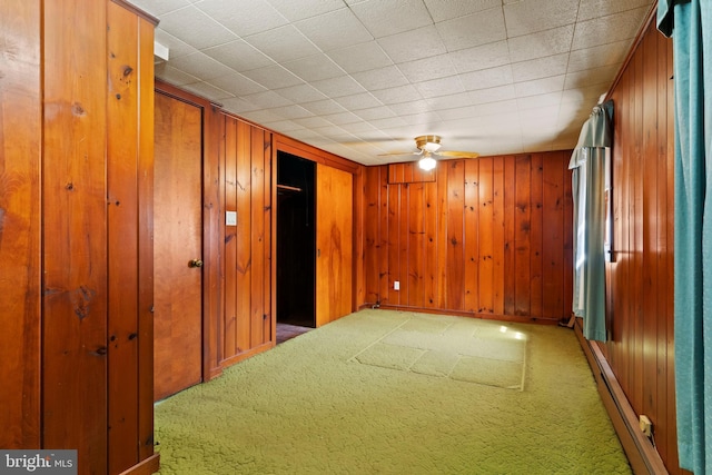 carpeted spare room with wood walls and a ceiling fan