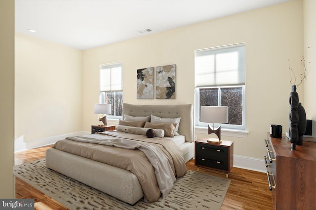 bedroom with wood finished floors, visible vents, and baseboards