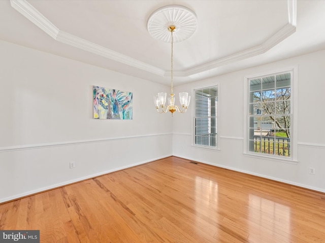 empty room featuring a raised ceiling, crown molding, a notable chandelier, and wood finished floors