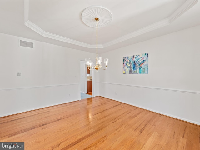 spare room with visible vents, a notable chandelier, ornamental molding, wood finished floors, and a raised ceiling