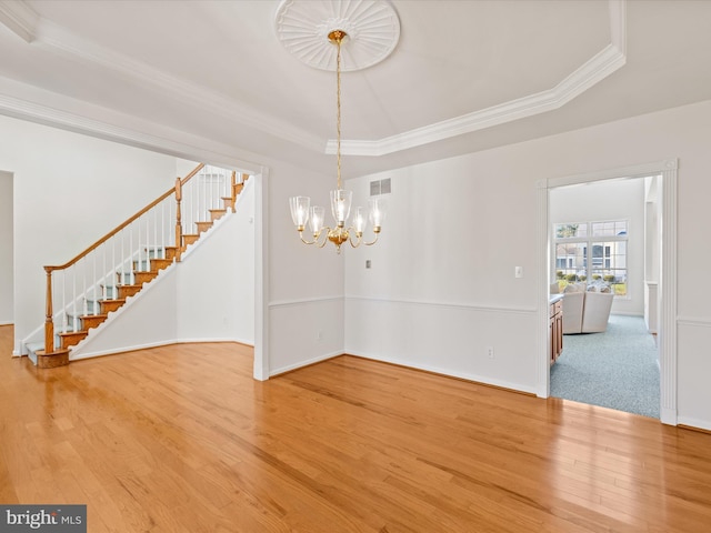 unfurnished dining area with wood finished floors, visible vents, a tray ceiling, stairs, and crown molding