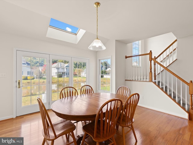 dining room with light wood finished floors, stairway, a skylight, and baseboards