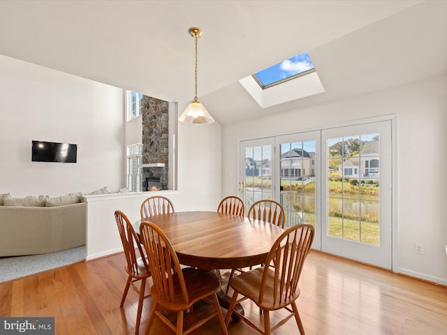 dining room with baseboards, vaulted ceiling with skylight, a stone fireplace, and light wood-style flooring