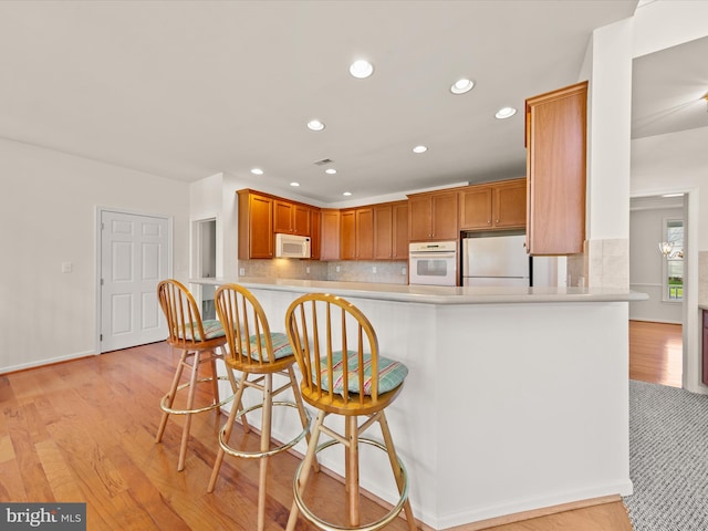 kitchen featuring decorative backsplash, white appliances, and light wood-style floors