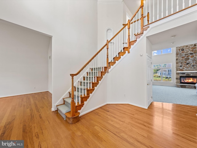 stairway with a stone fireplace, a high ceiling, baseboards, and wood finished floors