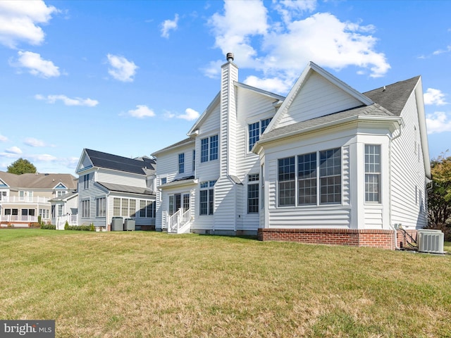 rear view of property featuring a lawn, central AC, a chimney, and roof with shingles