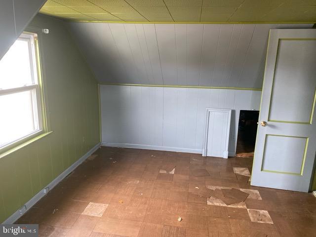 additional living space with baseboards, a healthy amount of sunlight, and vaulted ceiling