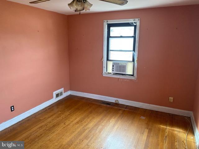 spare room with visible vents, wood finished floors, cooling unit, baseboards, and ceiling fan