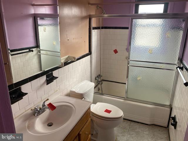 bathroom featuring bath / shower combo with glass door, tile walls, tile patterned flooring, and toilet