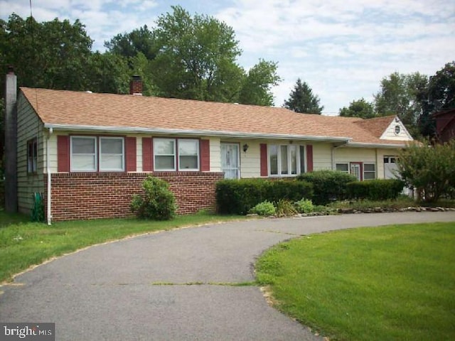 ranch-style house featuring a front yard, brick siding, and a chimney