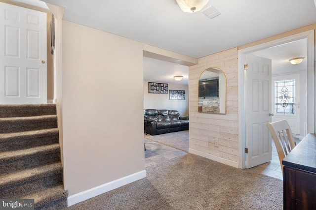 corridor with stairway, baseboards, wood walls, and carpet flooring