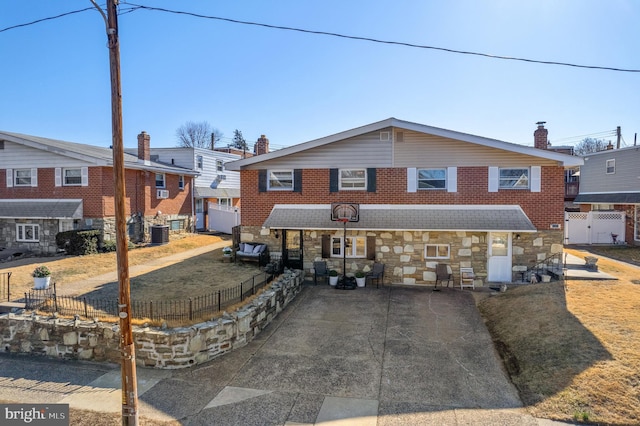 view of front of property featuring central AC unit, fence, concrete driveway, stone siding, and brick siding