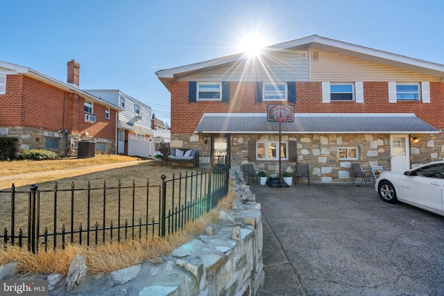 view of front of property with stone siding, concrete driveway, central AC, and fence